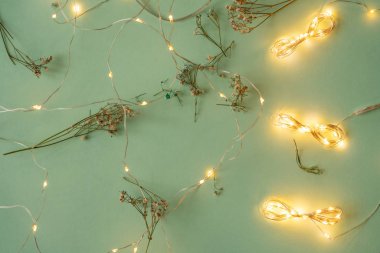 Açık yeşil arka planda Noel ışıkları, tatil çelengi ile yatıyordu
