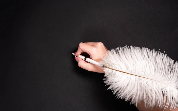 黒い表面に羽ペンを保持女性の手 — ストック写真