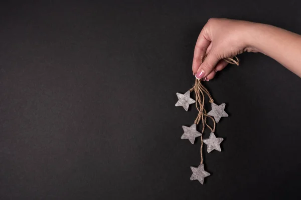 Weibliche Hand hält hölzerne Sterne mit Seil, flach über schwarzem Hintergrund — Stockfoto