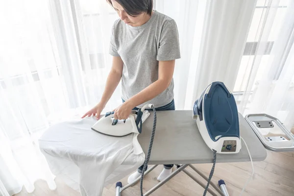 Mujer planchando camisa blanca a bordo de pie contra la ventana — Foto de Stock