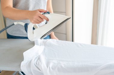 Ütü masasında beyaz gömlek ütüleyen kadın elleri