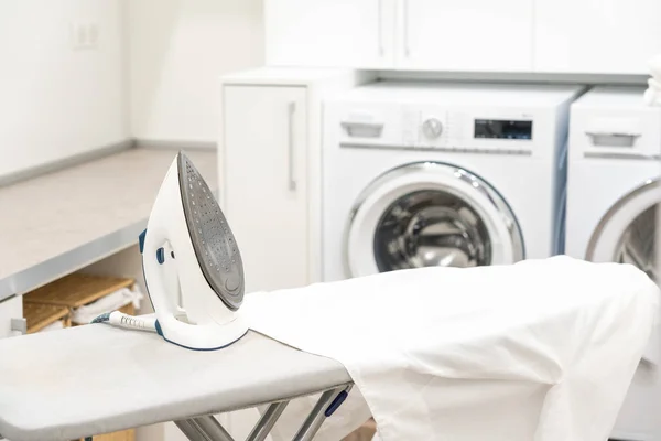 Deska do prasowania z białą koszulą i żelazkiem w pralni — Zdjęcie stockowe