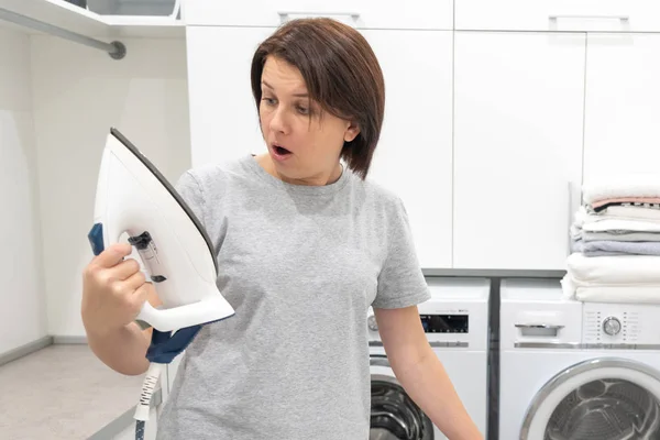 Mujer mirando con sorpresa al fondo de hierro roto en lavadero con lavadora sobre fondo — Foto de Stock