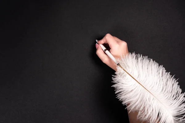 黒い表面に羽ペンを保持女性の手 — ストック写真