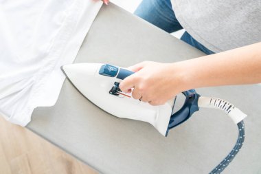 Ütü masasında beyaz gömlek ütüleyen kadın ellerinin üst görüntüsü