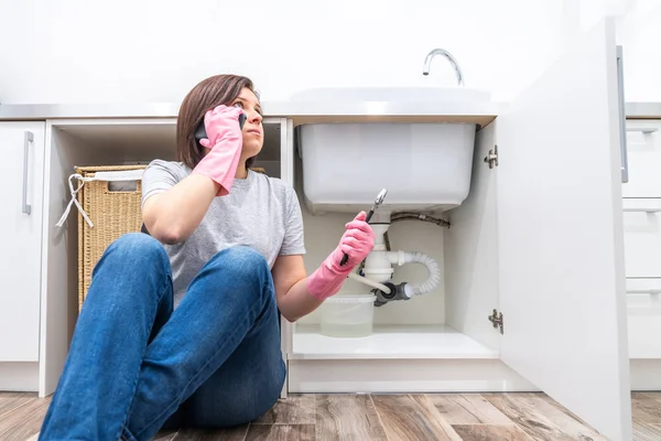 Woman sitting near leaking sink in laundry room calling for help