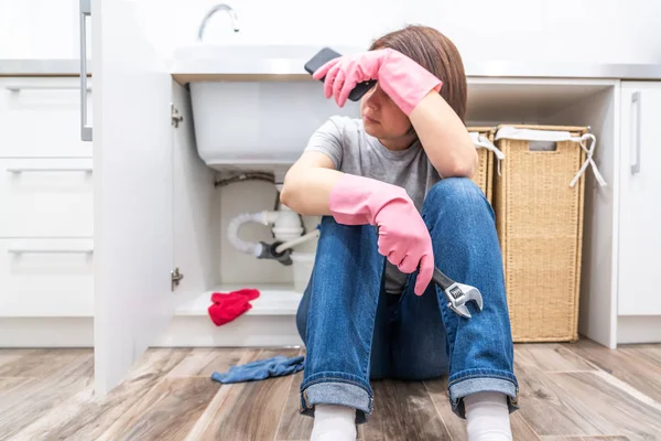 Woman sitting near leaking sink in laundry room holding adjustable wrench — Stock Photo, Image