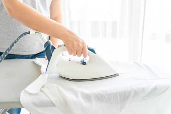 Mujer planchando camisa blanca en tabla de planchar — Foto de Stock