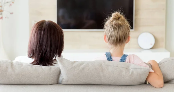 Mutter und Tochter sitzen auf dem Sofa und schauen fern, Familienzeitkonzept, Rückansicht — Stockfoto