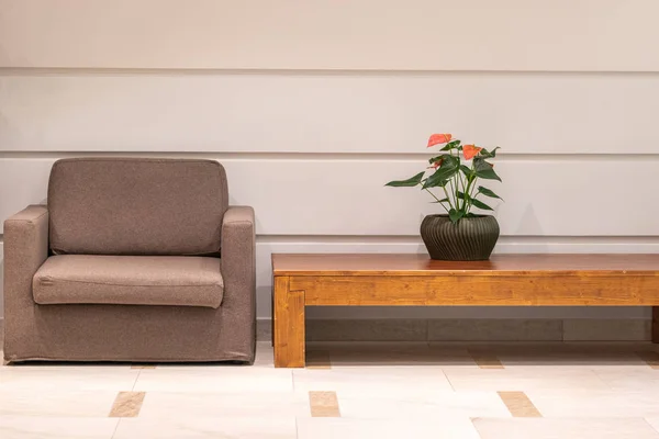 Interior de la sala del hotel con sillón marrón, mesa de madera y flor sobre fondo de pared blanco —  Fotos de Stock