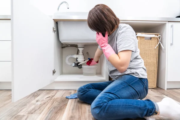 Woman sitting near leaking sink in laundry room calling for help — Stock Photo, Image