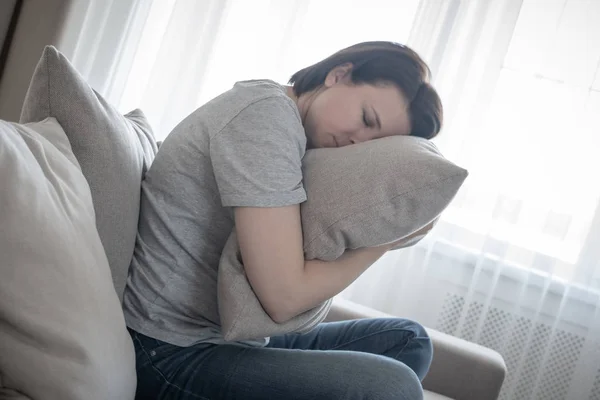 Evde üzgün bir kadın oturuyor ve yastığa sarılıyor, yalnızlık ve üzüntü kavramı. — Stok fotoğraf