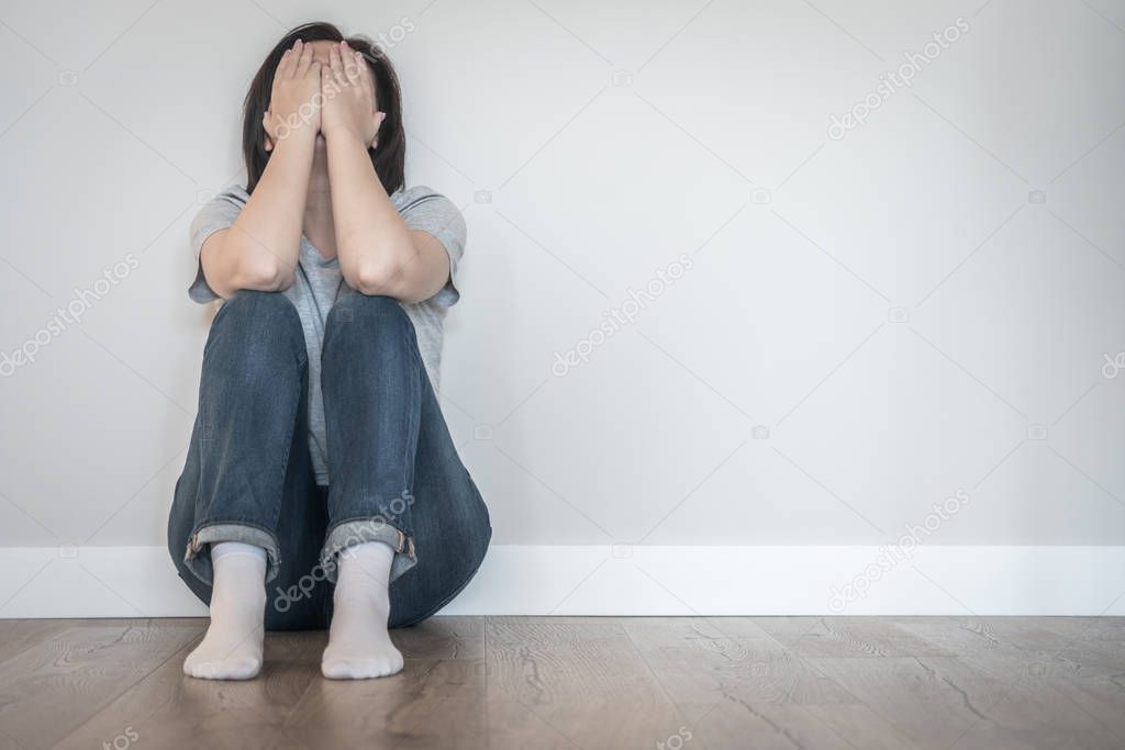 Sad woman sitting on a floor alone in empty room, despair and lonely concept with copy space
