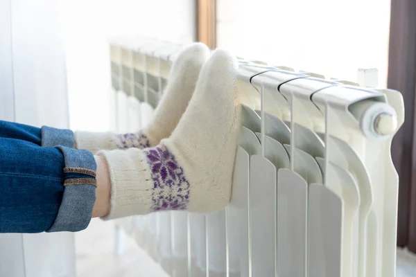 Woman warming up with feet on heater wearing woolen socks — 스톡 사진