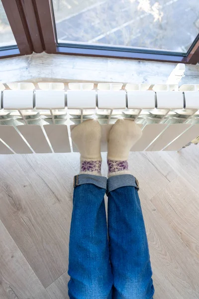 Woman warming up with feet on heater wearing woolen socks, view from above