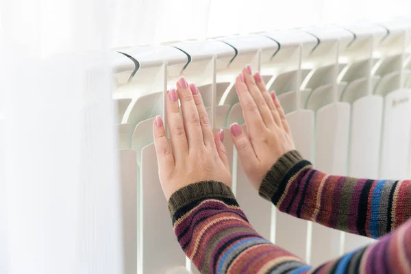 Chica calienta las manos congeladas por encima del radiador caliente, vista de cerca —  Fotos de Stock