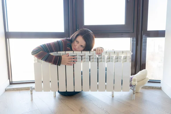 Woman wearing pullover sitting near heater radiator and hugs it — Stock Photo, Image