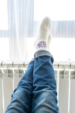 Isıtıcıda ayaklarıyla ısınan kadın yün çorap giyiyor.