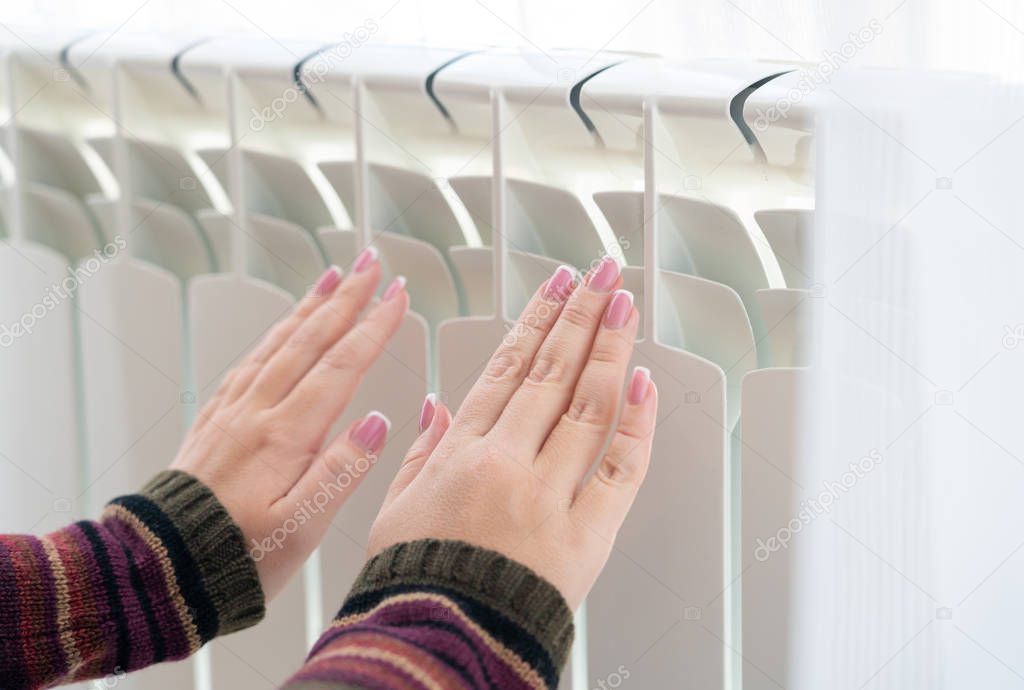 Girl warms up the frozen hands above hot radiator, close up view