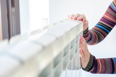 Ilık radyatöre iki eliyle dokunan kadın.