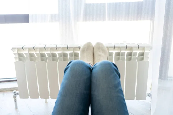 Woman warming up with feet on heater wearing woolen socks