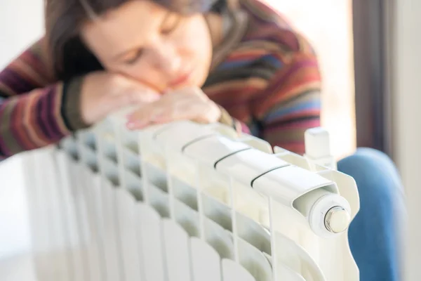 Žena v pulovru sedí u radiátoru a objímá ho. — Stock fotografie