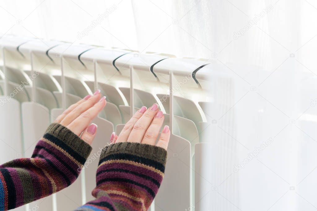 Girl warms up the frozen hands above hot radiator, close up view