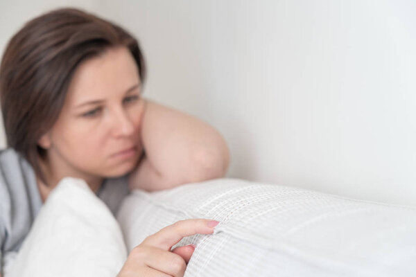 sad woman sitting on the bed holding pillow