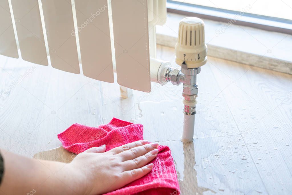 Female hand with rag cleaning water from heating radiator leak
