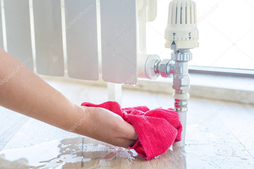 Female hand with rag cleaning water from heating radiator leak