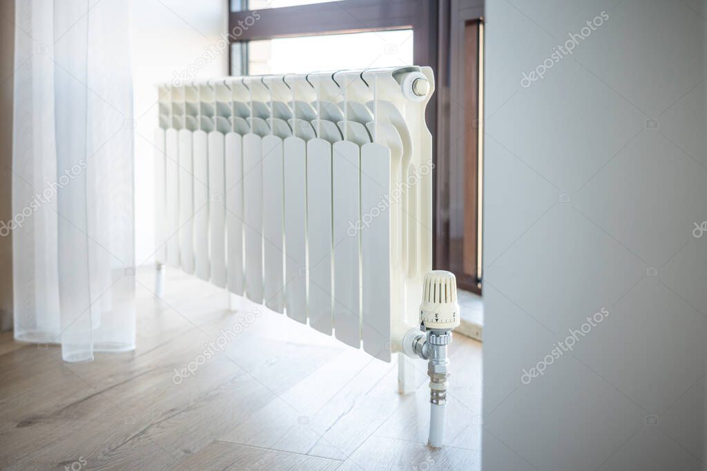 White big radiator with thermostat near window in modern room