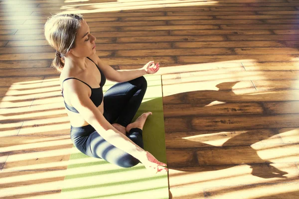 Young woman meditating sitting in lotus position against sunny window — Stock Photo, Image