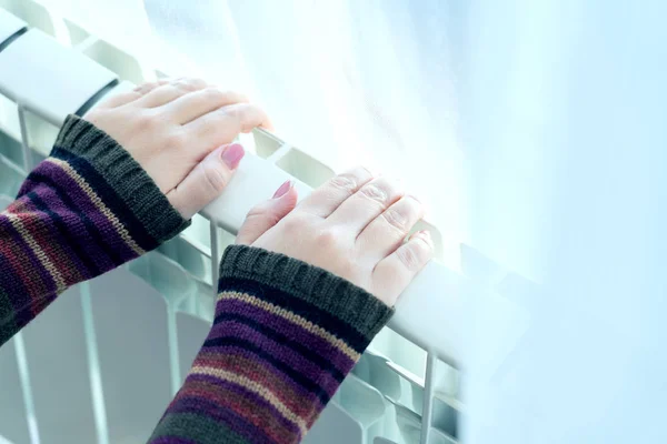 Dziewczyna rozgrzewa zamarznięte ręce nad ciepłą chłodnicą, widok z bliska, niebieskie tonizowanie — Zdjęcie stockowe