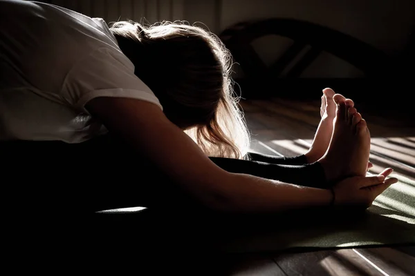 Jeune femme étirant dans la pose de yoga sur le tapis, silhouette dans l'obscurité — Photo