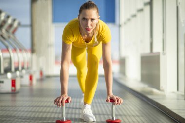 Spor salonunda kollarını ve kaslarını güçlendirmeye hazır, halterli, fiziki açıdan fit bir kadın.