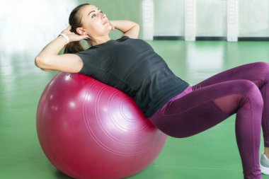 Spor salonundaki kadın sırtında pilates topuyla egzersiz yapıyor.