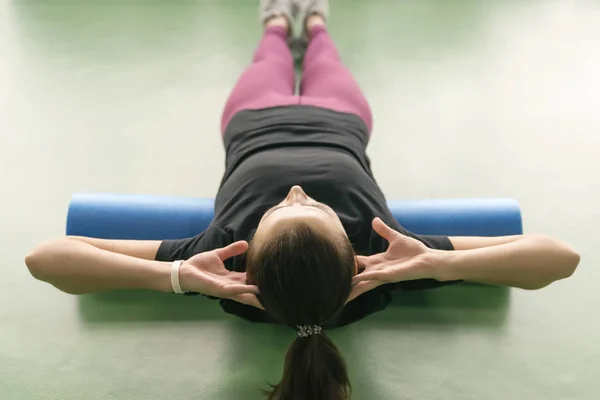 Привлекательная женщина делает упражнения с пеной на роликах расслабляет спину и позирует в современном ярком фитнес-центре — стоковое фото