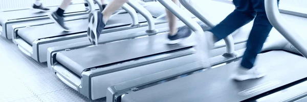 Ludzie biegający na maszynach, bieżnia z rozmyciem ruchu, niebieski ton — Zdjęcie stockowe