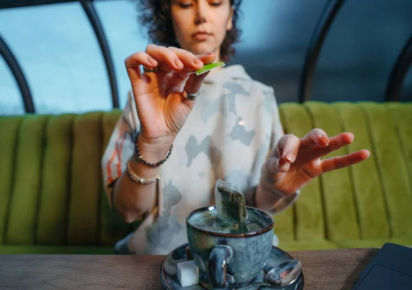 Kafede çay poşetiyle çay demleyen bir kadın.