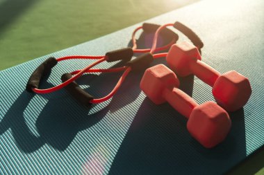 mat placed on floor with rubber expander and two dumbbells in fitness club