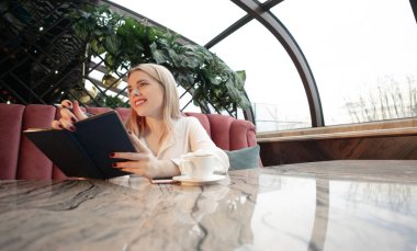 Genç kız gülümsüyor ve gelecekle ilgili planlarını ve amaçlarını kendi günlüğünde yazıyor.