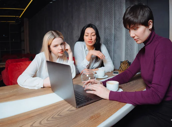Üç genç iş kadını dizüstü bilgisayarlarıyla masada oturuyor ve kafede bir proje üzerinde çalışıyorlar. Takım çalışması, iş toplantısı. Serbest çalışanlar. — Stok fotoğraf
