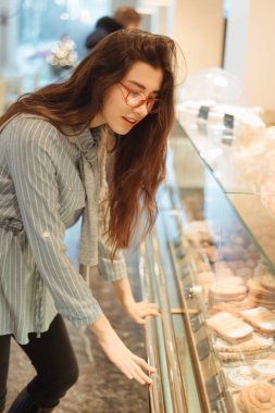 Uzun saçlı güzel bir Asyalı kız pencerenin yanındaki kafede tatlı seçiyor. Pastanenin içi çok güzel.