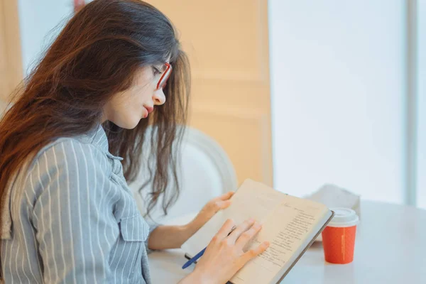 Приваблива молода жінка робить нотатки в блокноті, насолоджуючись відпочинком у стильному кафе — стокове фото