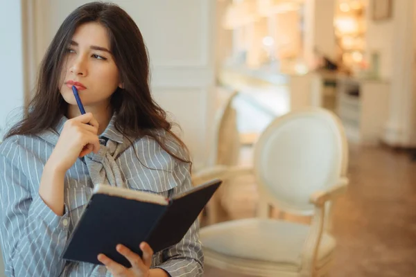 Продумана молода жінка тримає блокнот і думає про творчі ідеї для написання есе в кафе — стокове фото