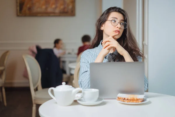 Portret młodej freelancerki korzystającej z laptopa do pracy na odległość, siedzącej we wnętrzu nowoczesnej kawiarni, inteligentnej kobiety pracującej nad książką internetową podczas porannego śniadania w kawiarni — Zdjęcie stockowe