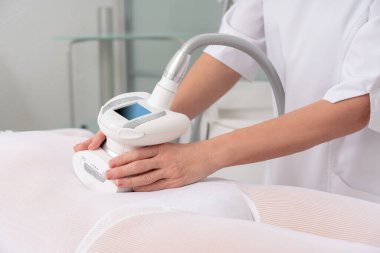 Beyaz takım elbiseli bir kadın spa salonunda selülit karşıtı masaj yaptırıyor. Klinikte LPG ve vücut şekillendirme tedavisi.