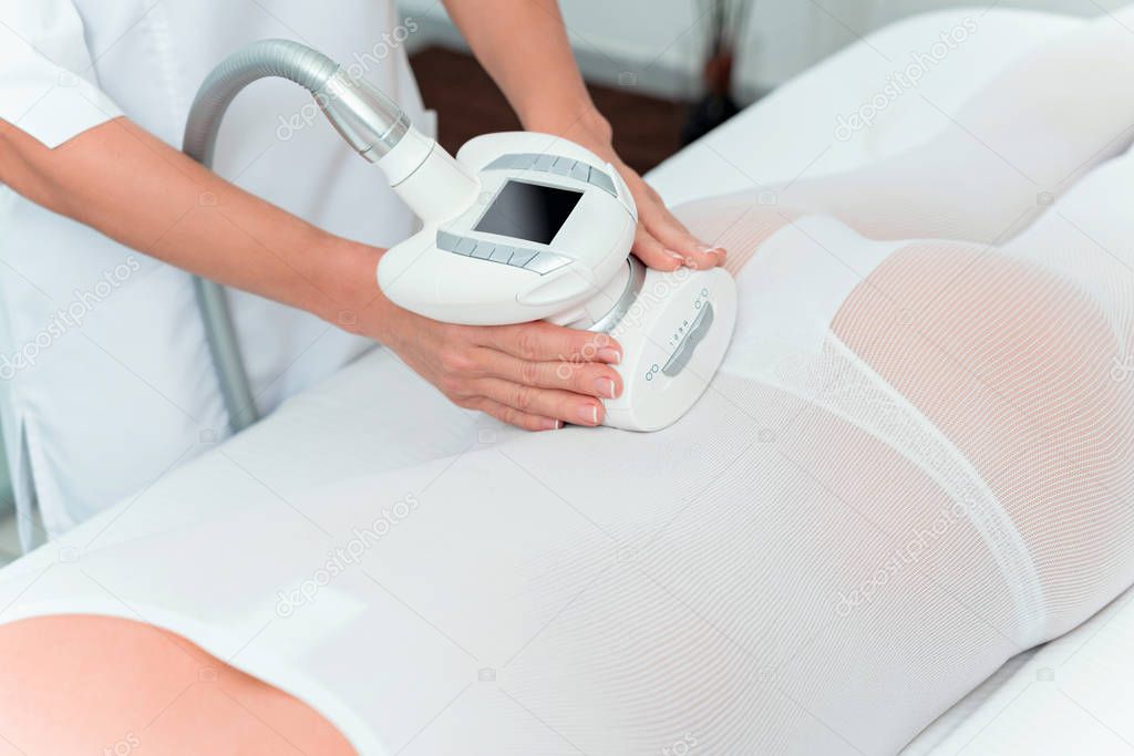 Woman in special white suit getting anti cellulite massage in a spa salon. LPG, and body contouring treatment in clinic.