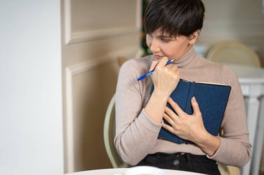 Kalem ve not defteri olan çekici genç bir kadın şık bir kafede yeni fikirler düşünürken gülümsüyor.