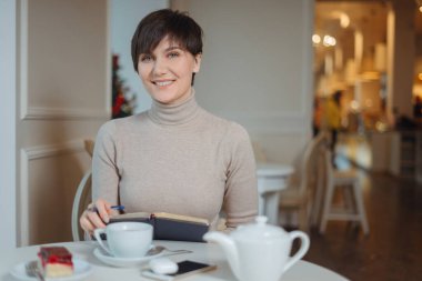 Elinde kalem olan çekici genç bir kadın. Şık bir kafede boş vakitlerin tadını çıkararak not defterine yazacak planlar ve listeler düşünüyor.